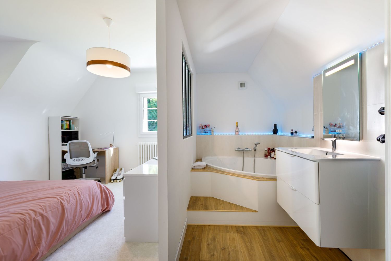 Chambre avec salle de bains attenante ouverte, comprenant une baignoire, un meuble lavabo suspendu et un chaleureux parquet en bois