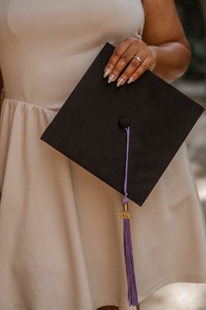Close-up of a hand holding a black graduation cap with purple tassel and 2025 charm.