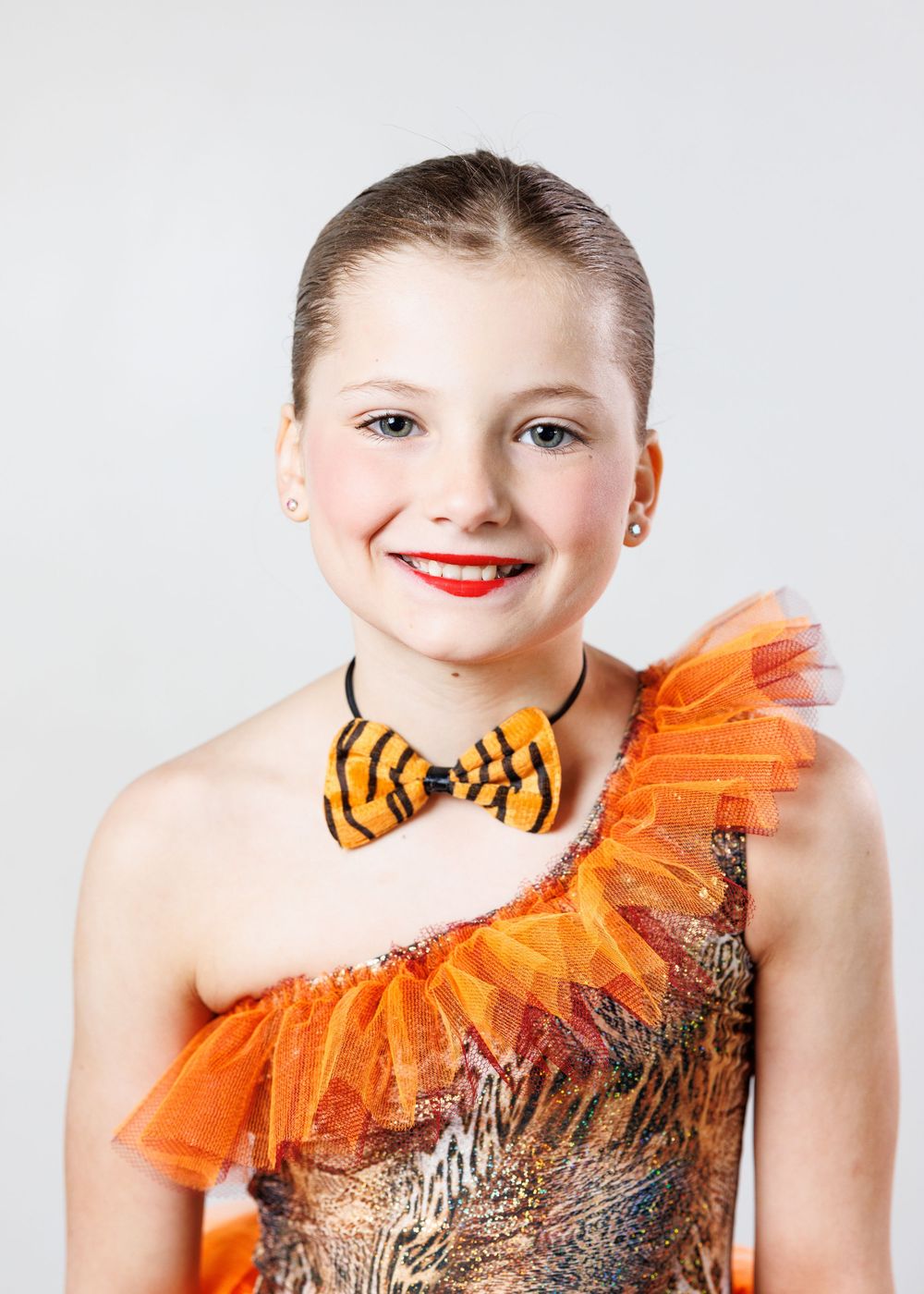 Young girl in orange tiger-striped dance costume with bow tie and tulle, smiling for a portrait photo.