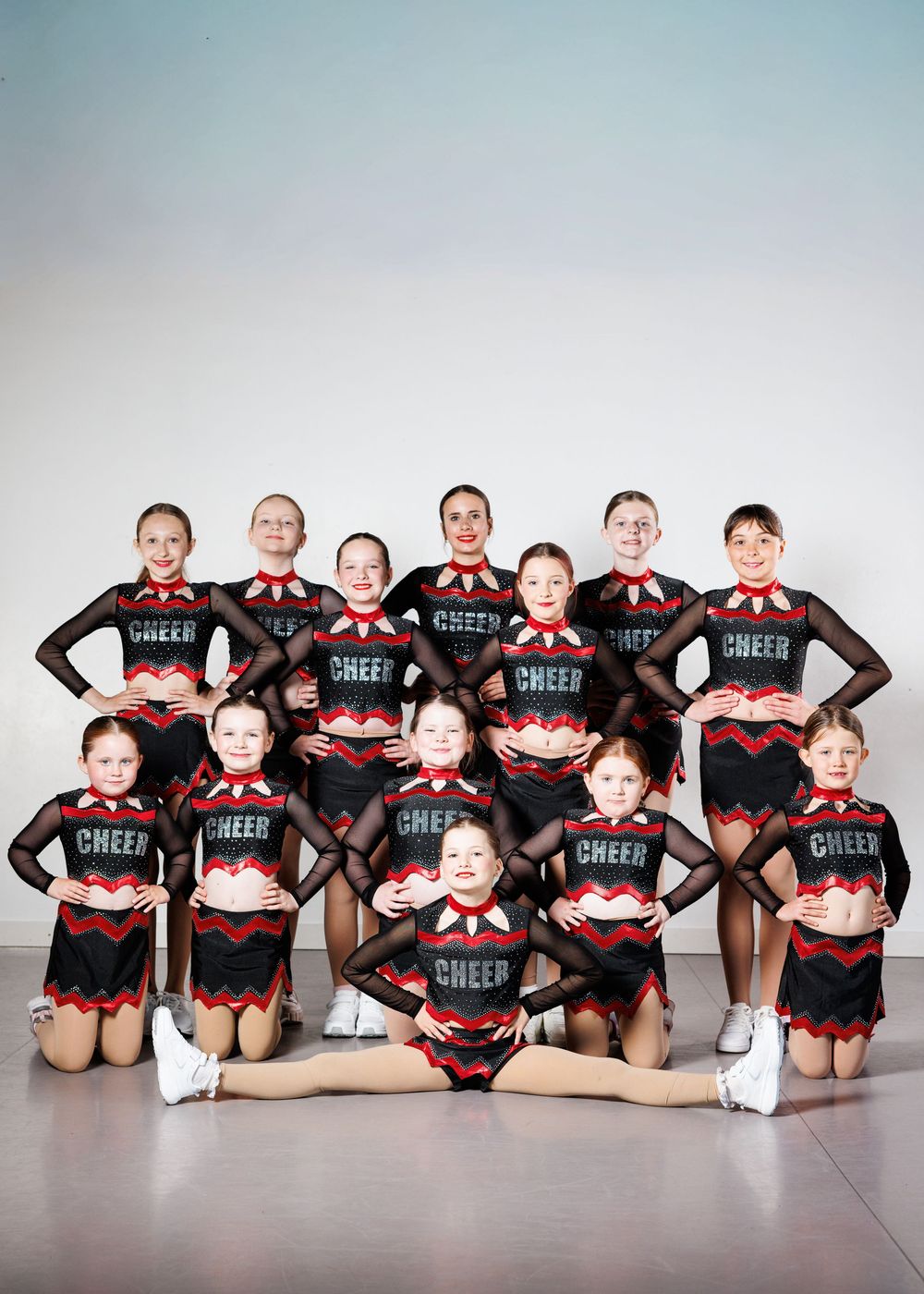 Youth cheerleading squad posing in black and red CHEER uniforms for a team photo in two rows.