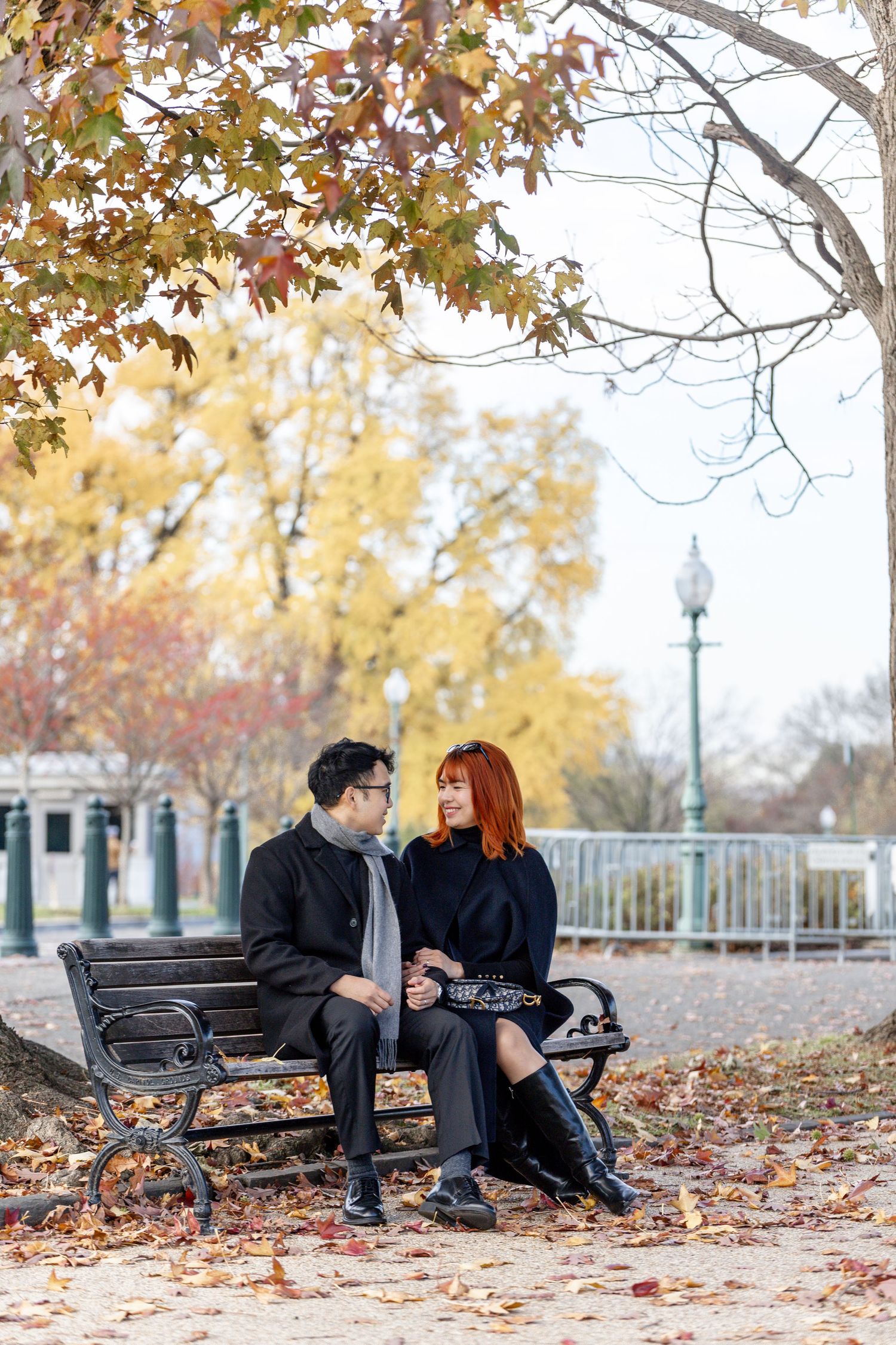 Couple embracing in front of US Capitol building surrounded by vibrant autumn foliage, woman in white dress, man in suit.