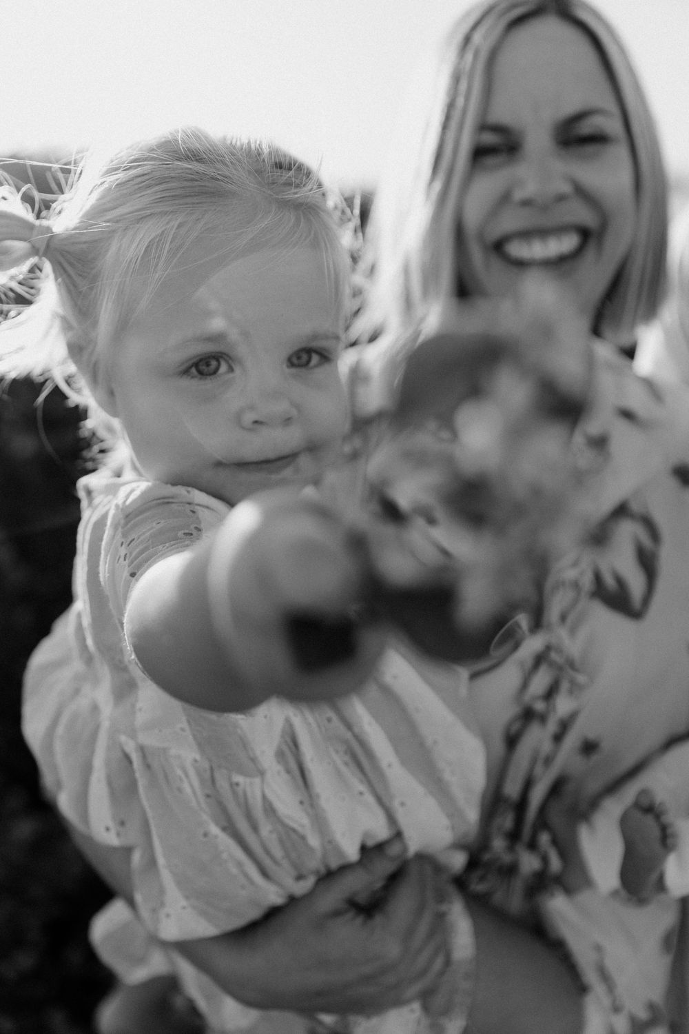 Black and white photo of a smiling woman holding a young blonde girl reaching toward the camera.