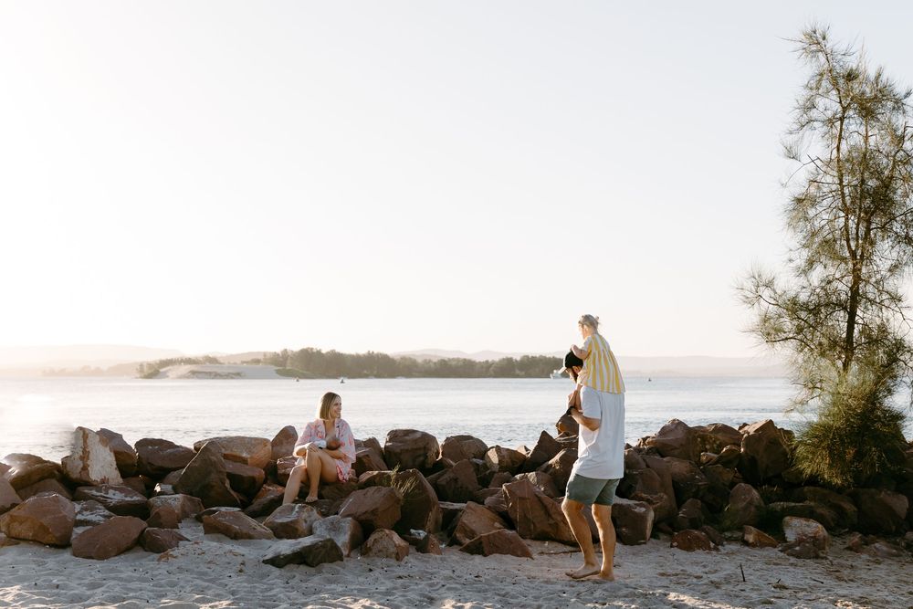 Family relaxing on rocky beach shore with calm ocean views on a sunny day.