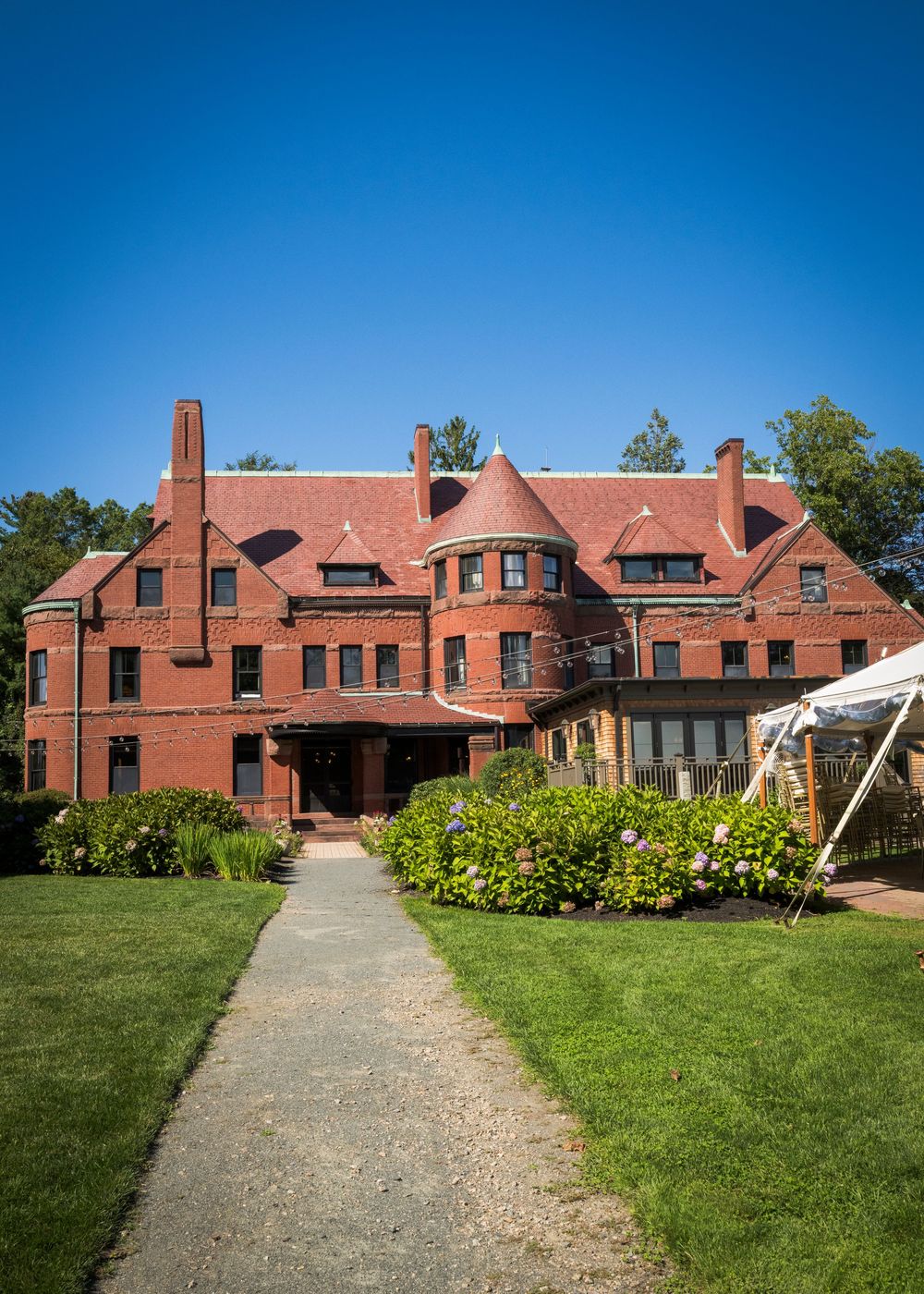 A grand red brick Victorian mansion with turrets, multiple chimneys, and lush green gardens under a clear blue sky.