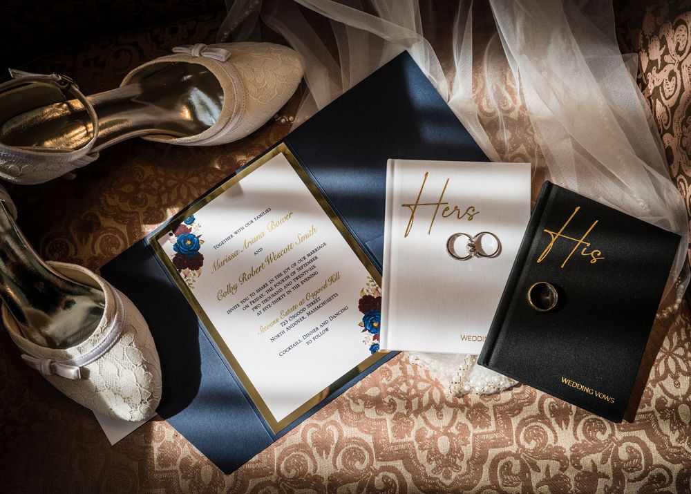Elegant wedding stationery flat lay with navy blue invitation suite, Hers and His vow books, rings, and bridal heels.