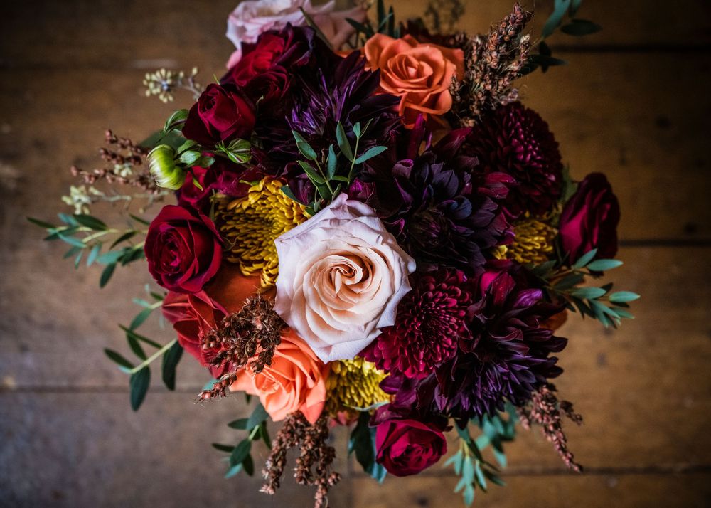 Lush autumn wedding bouquet with deep red, burgundy, peach, and gold flowers on rustic wood.