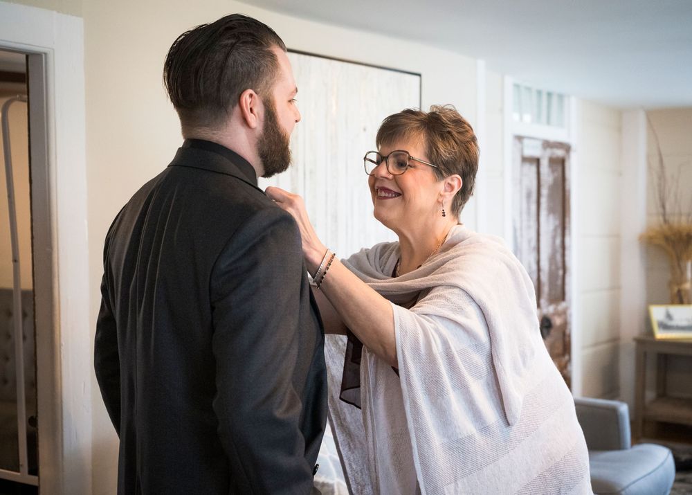 Older woman lovingly adjusting groom's suit jacket before wedding ceremony.