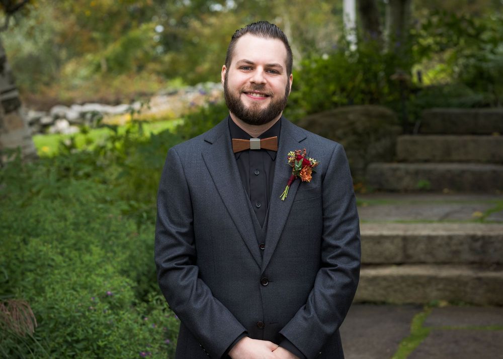 Smiling groom in dark suit with floral boutonniere posing outdoors before wedding.