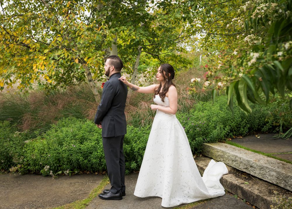 Bride adjusting grooms boutonniere during first look in a lush green garden setting.