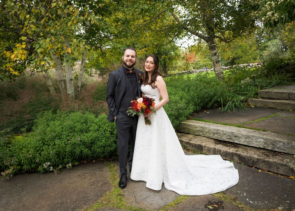 Bride and groom posing together in a garden with autumn foliage during wedding portraits.