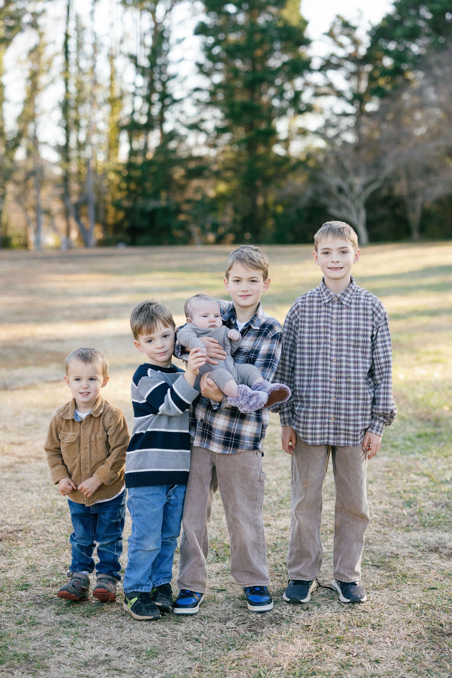 Parents holding infants while standing together on a hillside near a wooden fence.