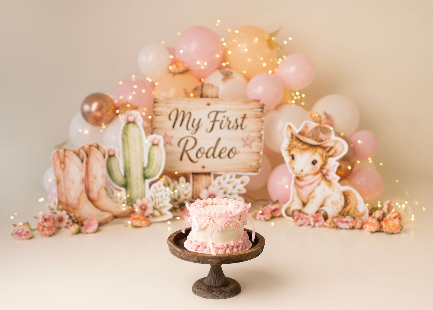 My First Rodeo cake smash setup with pink balloons, cowboy boots, cactus, and a sweet cowgirl bear backdrop.