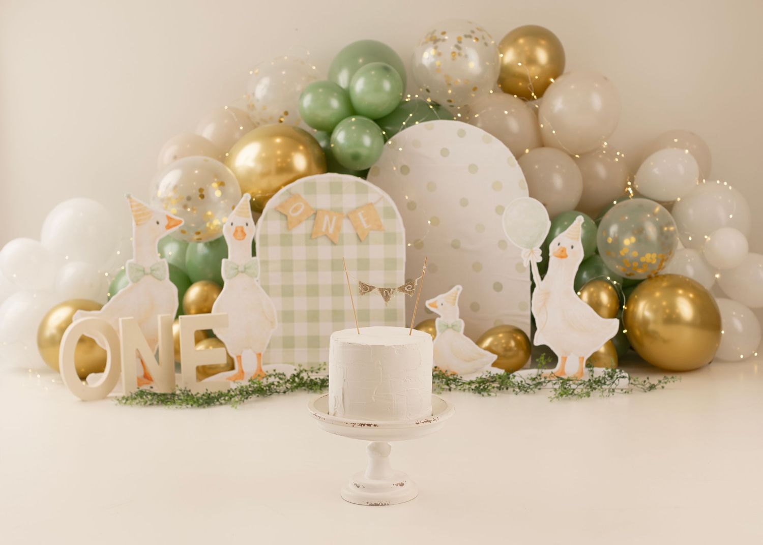 First birthday cake smash setup with sage green, gold, and white balloon arch.