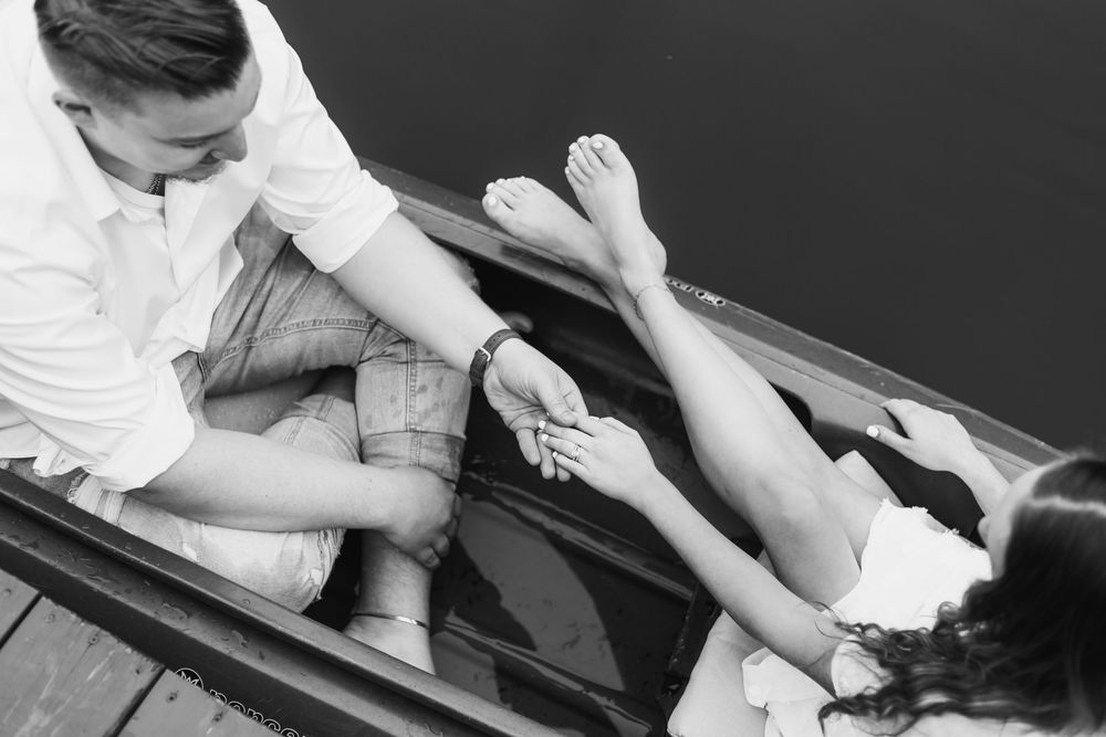 Black and white photo of a couple relaxing on a wooden dock, legs intertwined over the water.