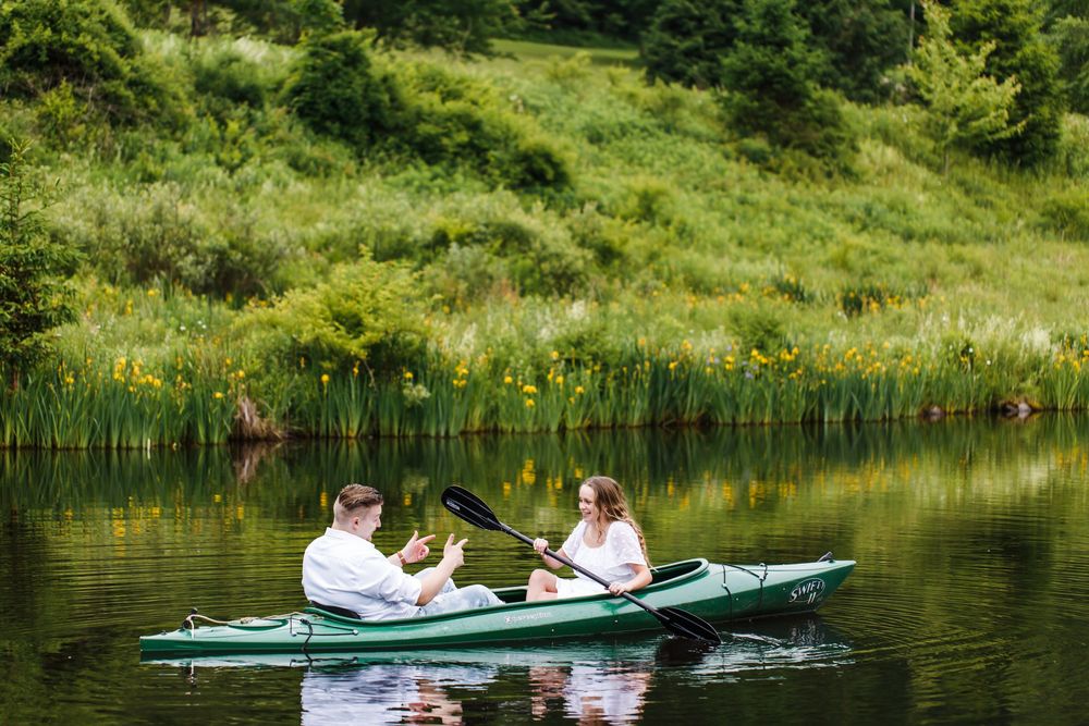 Couple kayaking together on a calm green lake surrounded by lush vegetation on a sunny day.