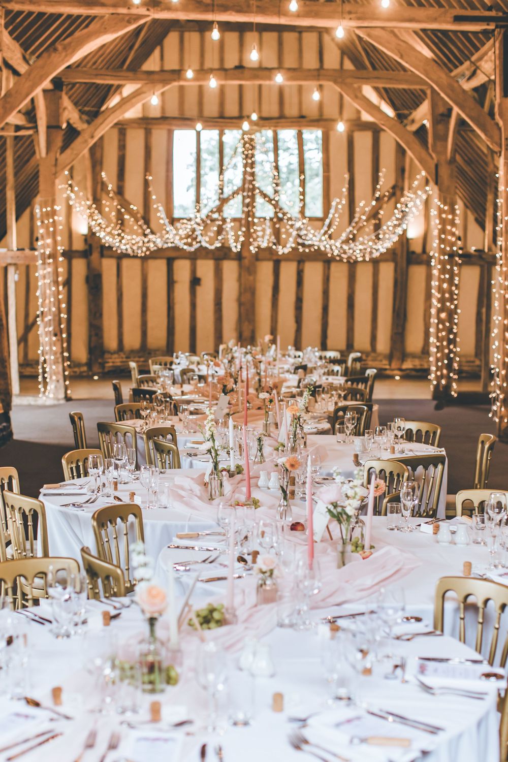Elegant barn wedding reception with fairy lights, round tables with pink floral centerpieces and candles.