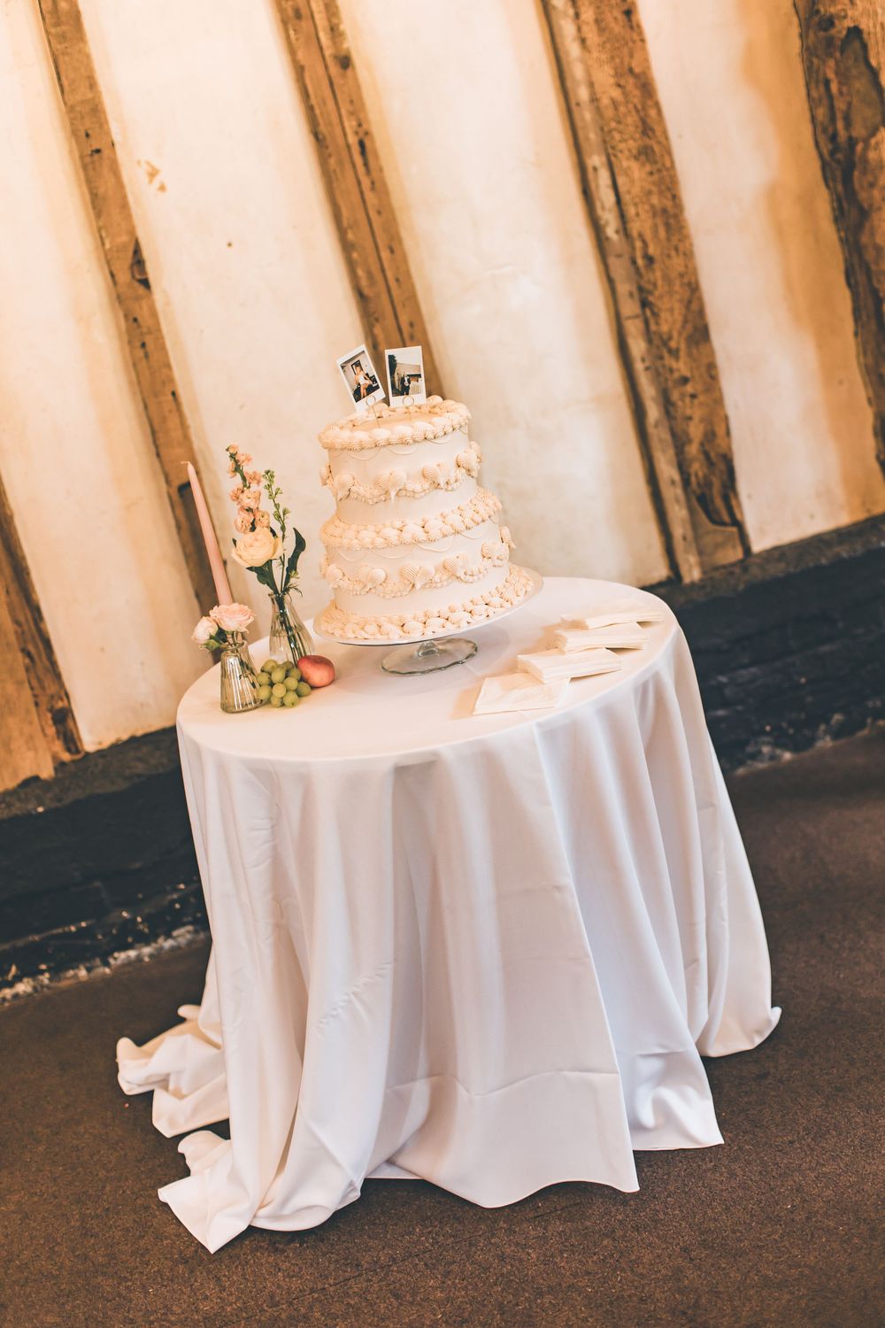 White multi-tiered wedding cake with ruffled decoration displayed on a round table with white satin tablecloth.