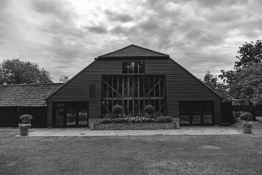Black and white photo of a large traditional barn with wooden facade under dramatic cloudy skies.
