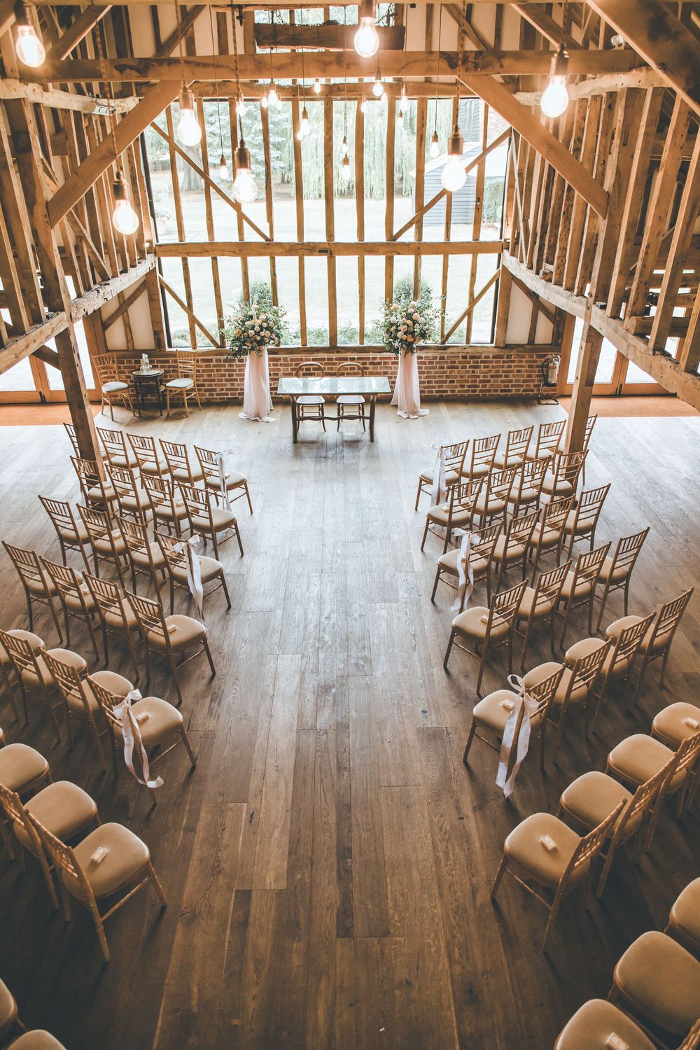 Rustic barn wedding ceremony setup with wooden chairs arranged in rows, exposed timber beams, and floral altar decorations.