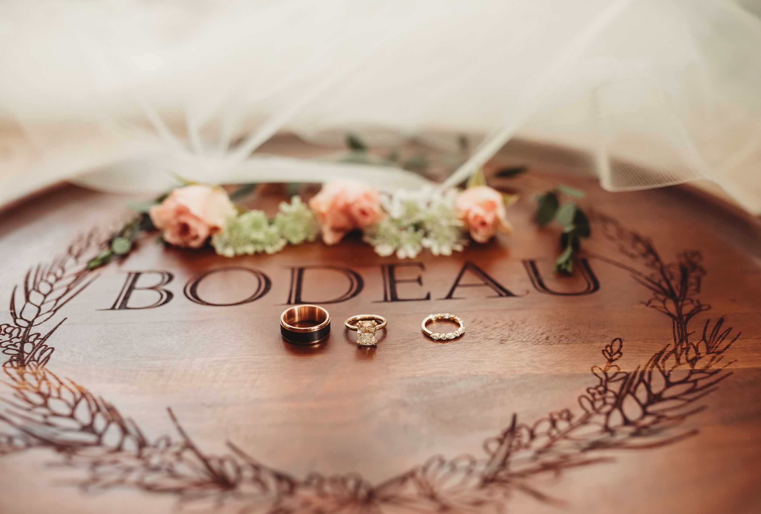 Wooden engraved Bodeau wedding ring dish with gold bands and floral wreath decoration under a bridal veil.