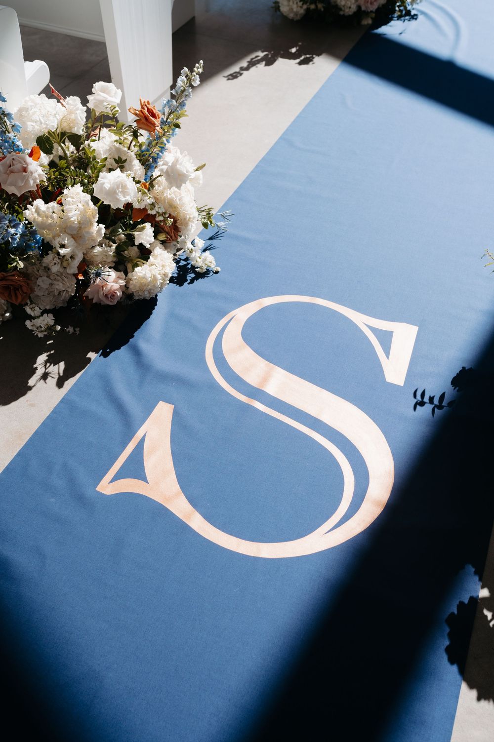 Blue aisle runner with elegant monogram letter S, adorned with white and blue floral arrangements at a wedding ceremony.