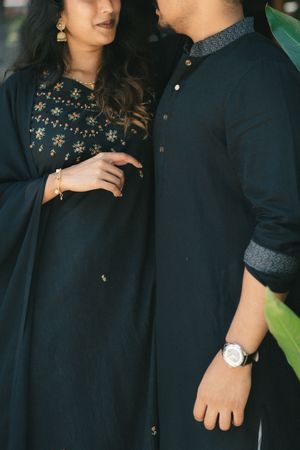 Couple in matching black traditional Indian outfits, woman in embroidered kurta with dupatta, man in kurta with watch.