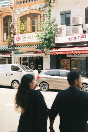 Couple holding hands on a busy street in front of Rojak Times restaurant in a vibrant Asian city.