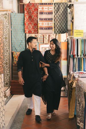 Couple in black traditional Indian attire shopping for colorful fabrics and Pashmina shawls in a textile store.