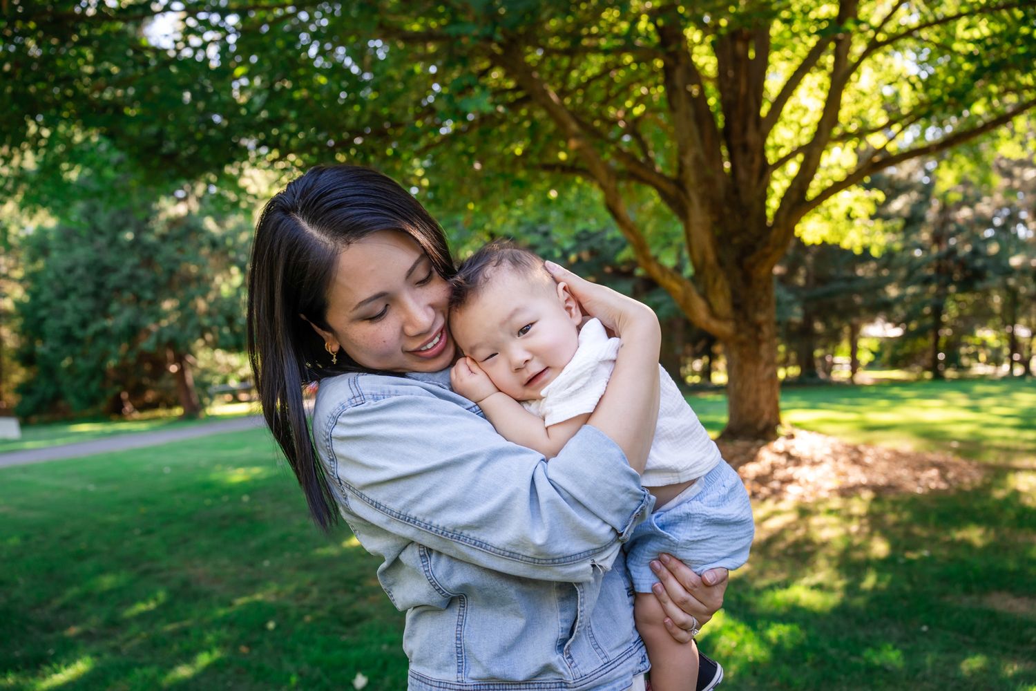 Mom cuddling baby boy with a tree in the background