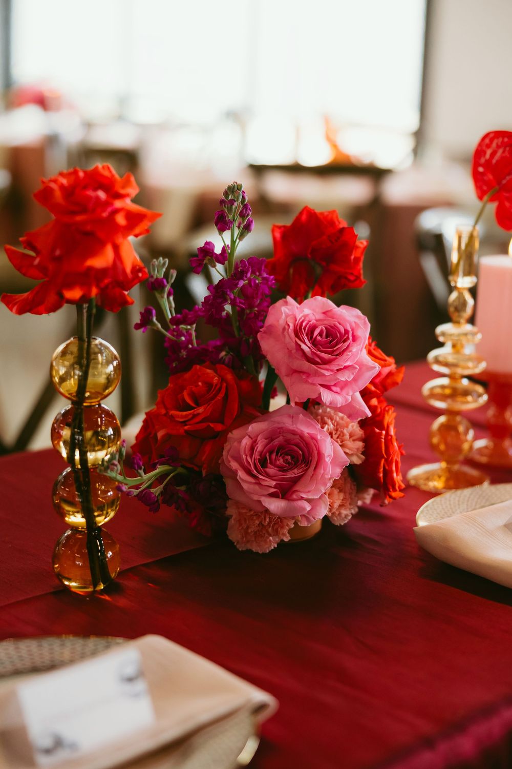 Red and pink rose centerpiece with purple blooms on a crimson tablecloth at an elegant wedding reception.