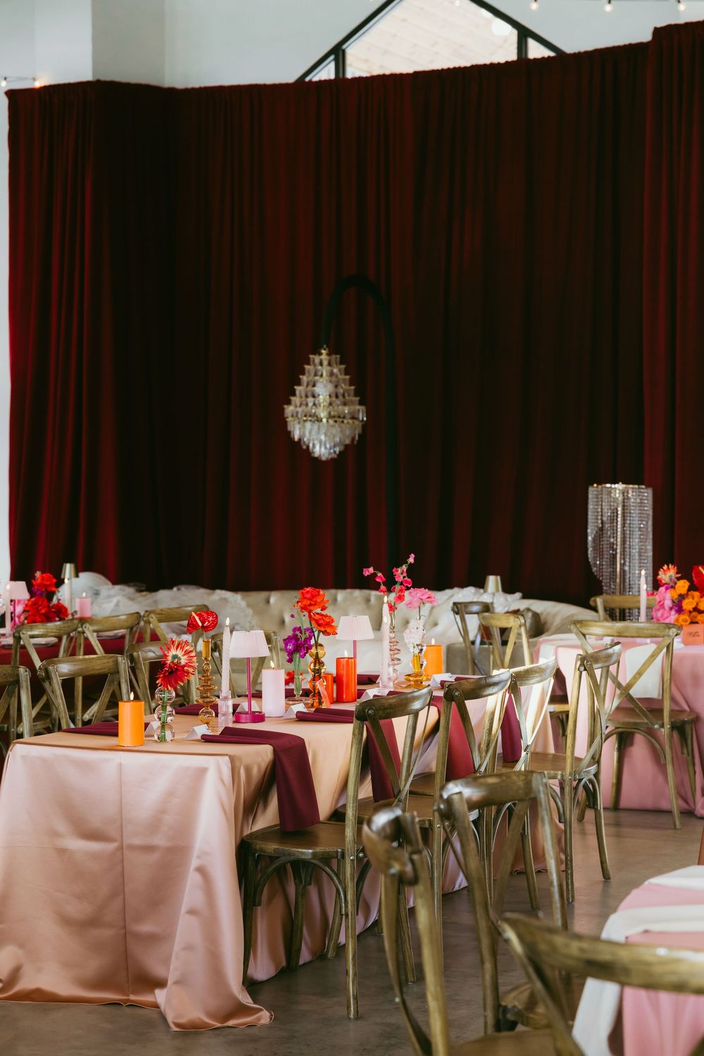 Romantic wedding reception with pink and burgundy linens, colorful floral centerpieces, and a crystal chandelier.