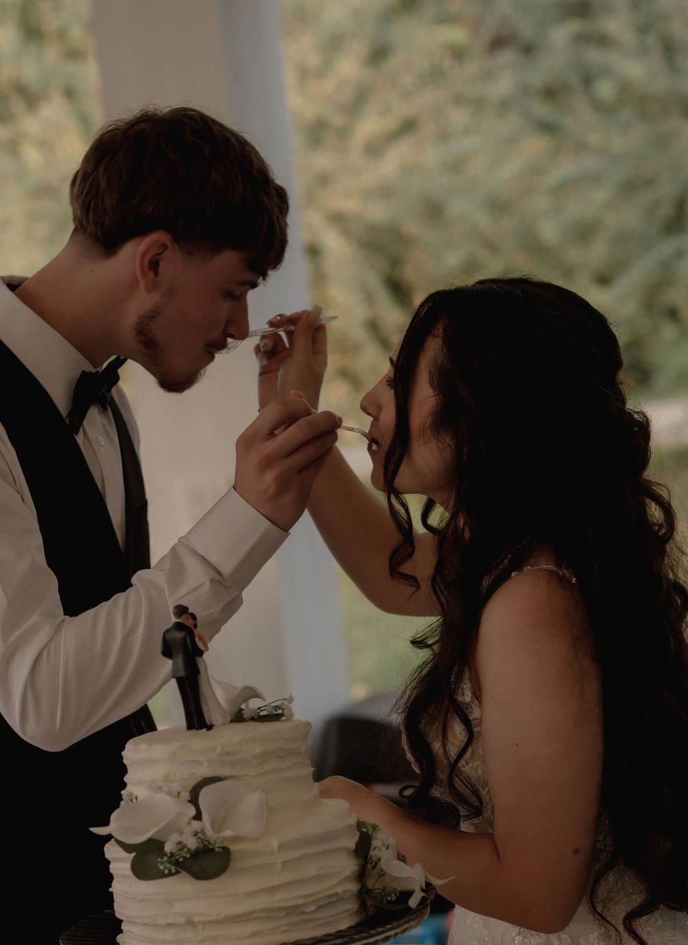 Bride and groom feeding each other wedding cake at their elegant white-frosted cake cutting ceremony.
