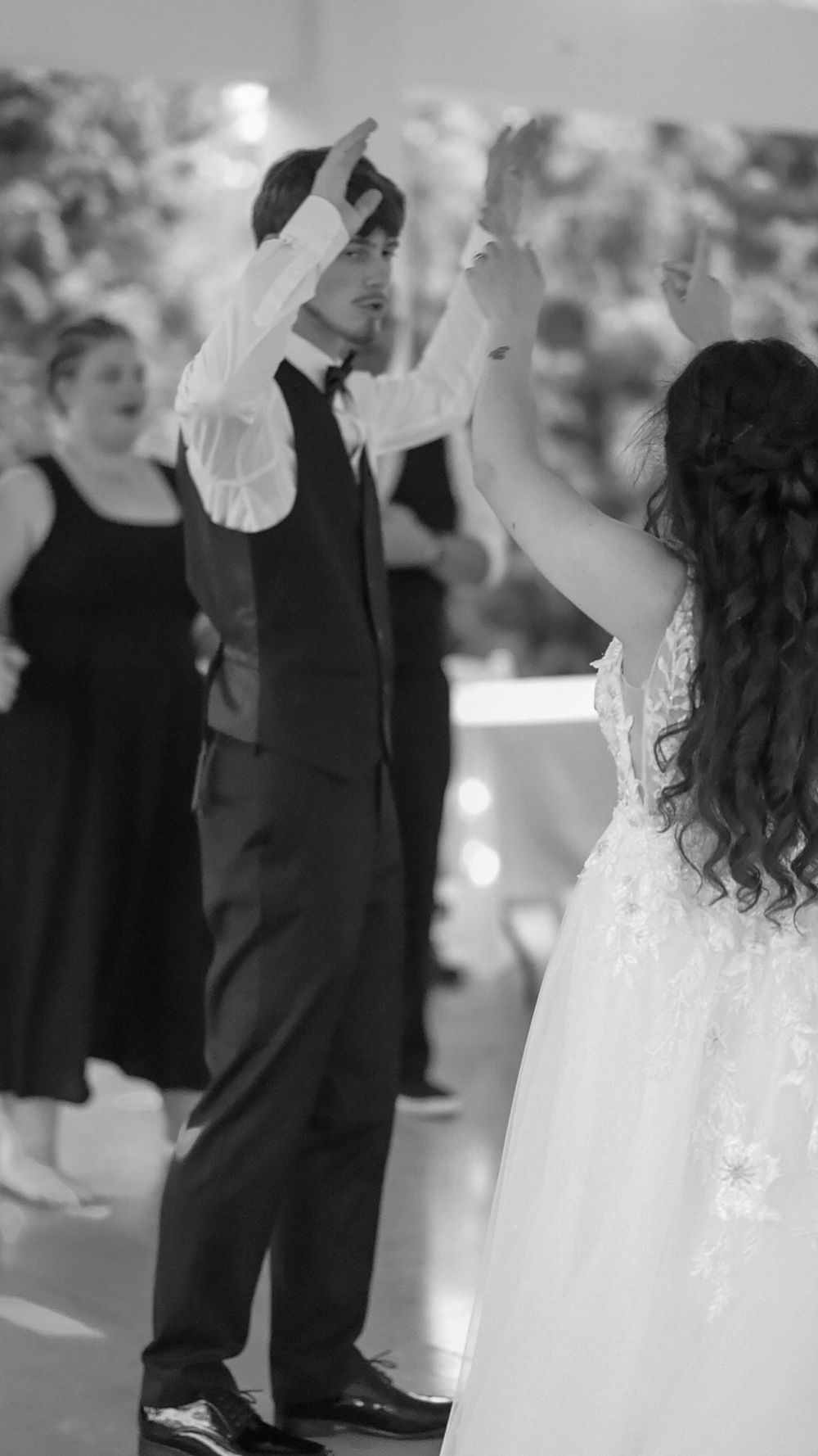 Black and white photo of bride and groom raising hands joyfully during energetic wedding reception dance.
