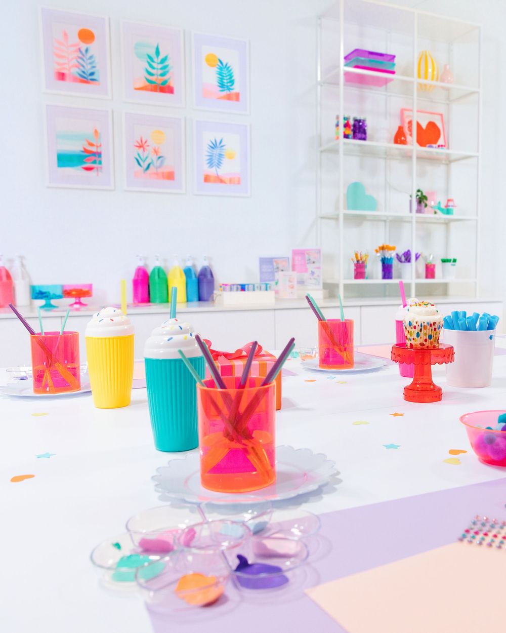 Colorful party table setup with neon cups, mini cakes, and confetti in a bright white studio space.