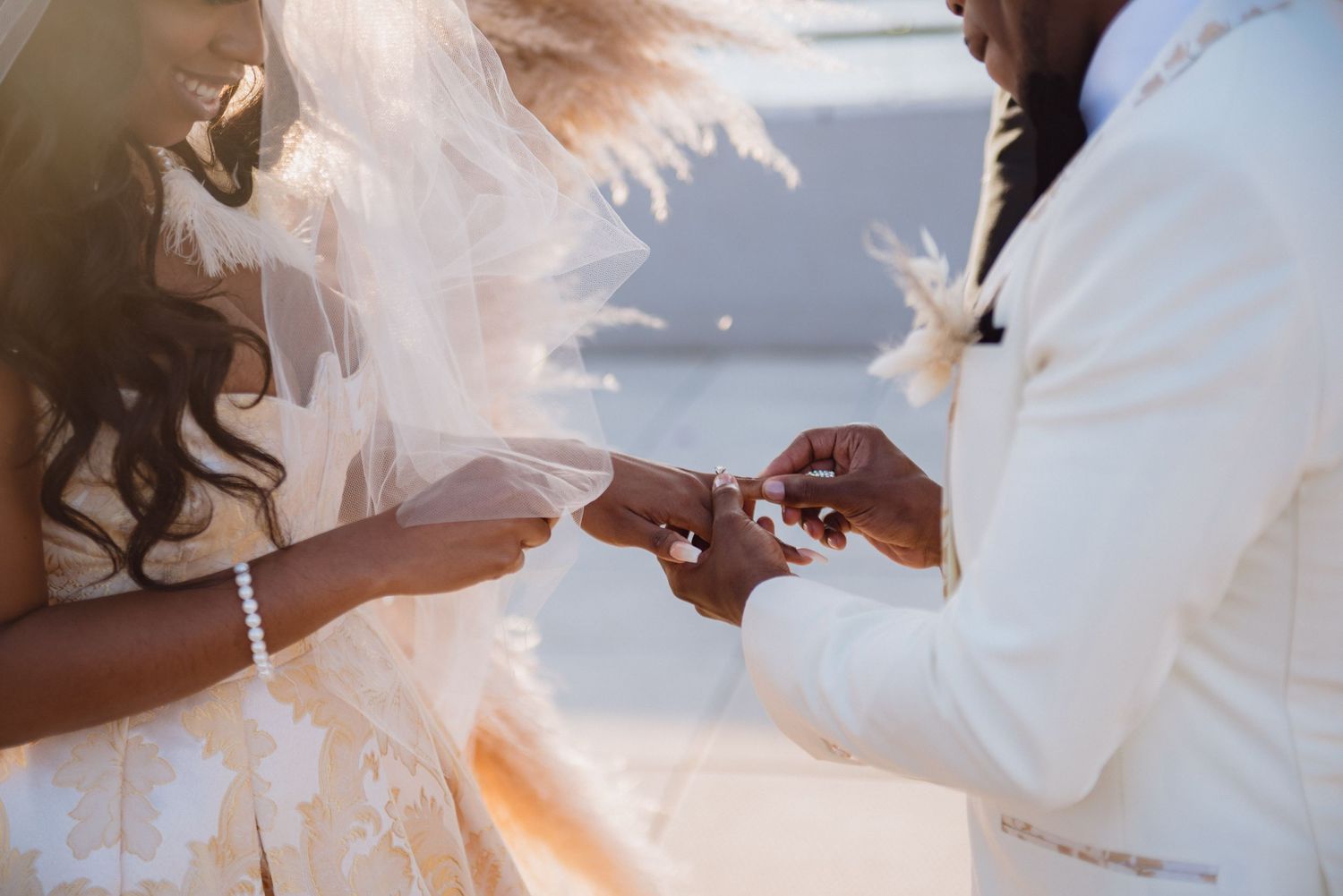 Close-up shot of hands exchanging rings during a sunlit outdoor ceremony.