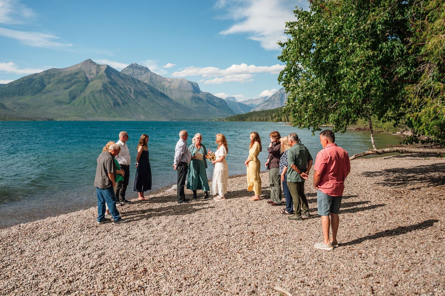 Small wedding ceremony on a rocky lakeshore with mountain backdrop at Glacier National Park.