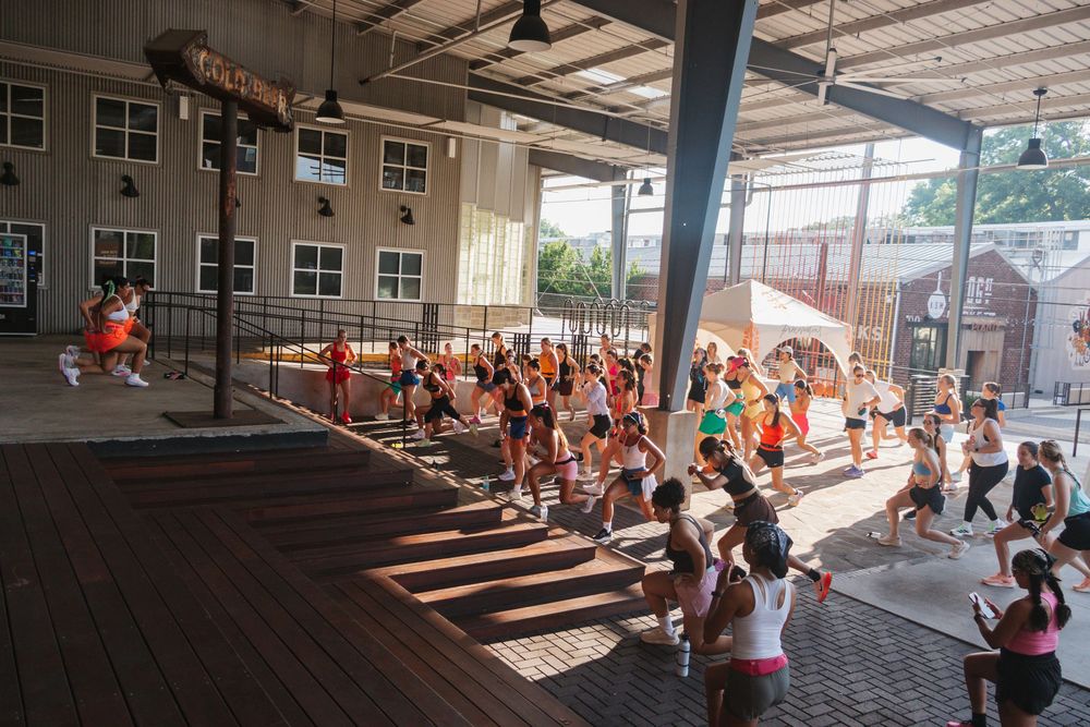 Large group of people participating in an outdoor fitness class on a wooden deck at a modern open-air venue.