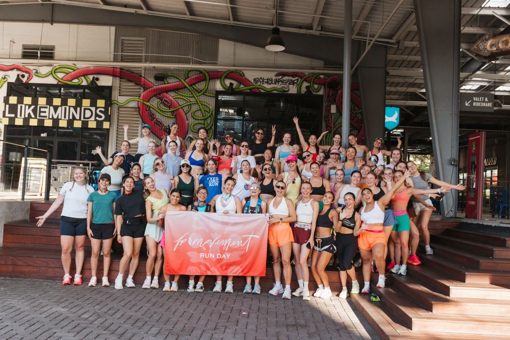 Large group of athletes posing together outside a LikeMinds venue, holding a colorful banner at a running event.