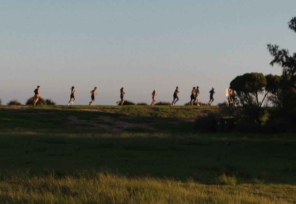 Silhouetted runners jogging along a grassy hilltop ridge at dusk in an open field landscape.