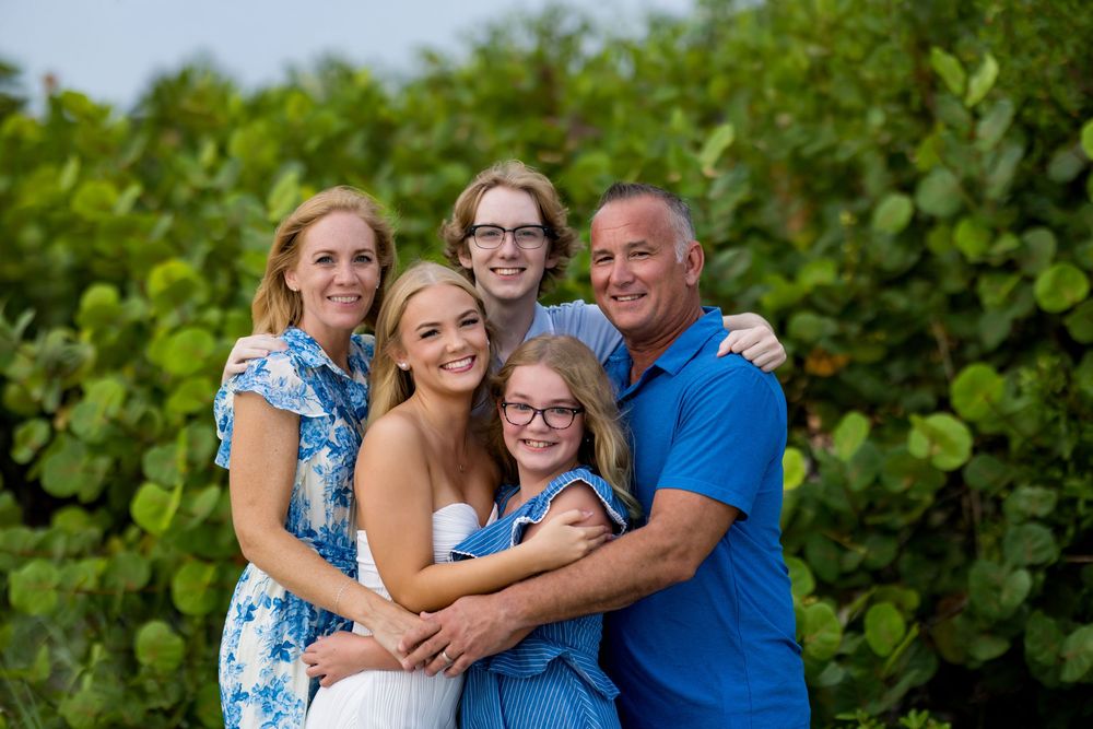 Happy family of five smiling together outdoors with lush green tropical foliage in the background.