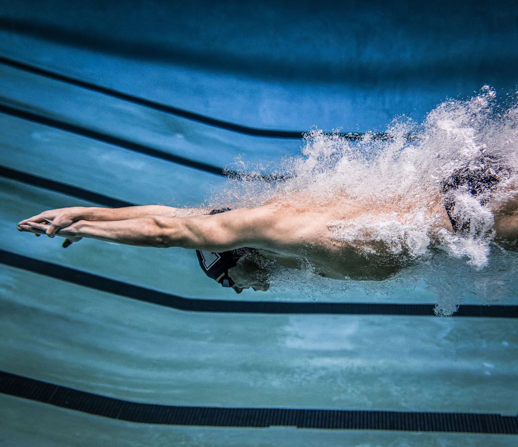 Competitive swimmer performing butterfly stroke underwater in a pool, captured mid-stroke with dynamic water splash.