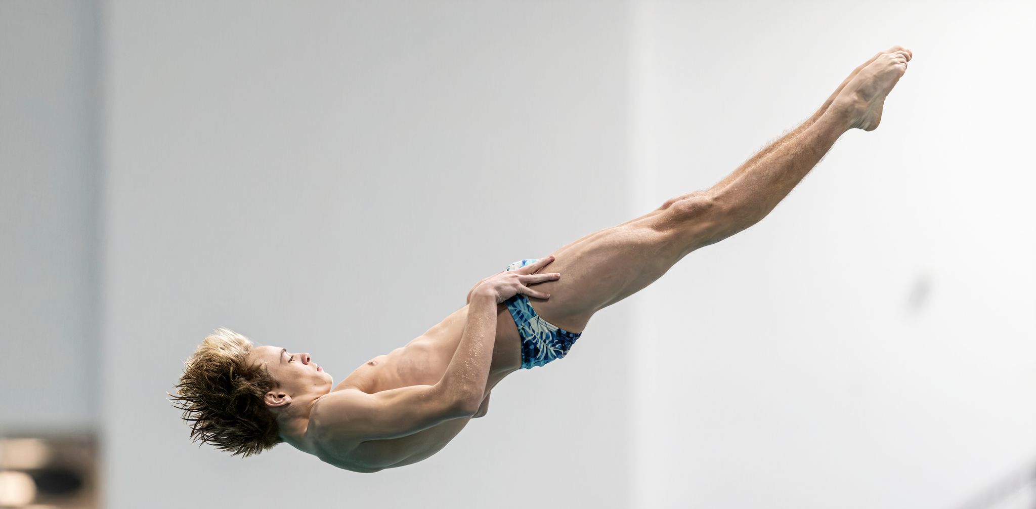 Male diver mid-air in a swan dive position during a competitive diving event.