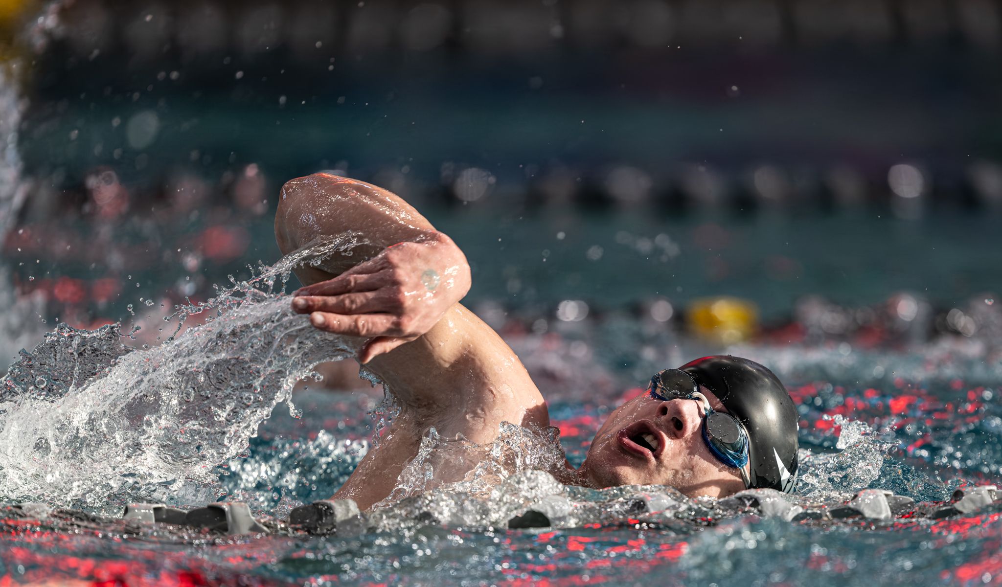 Competitive swimmer performing freestyle stroke in pool, wearing goggles and cap, water splashing around them.