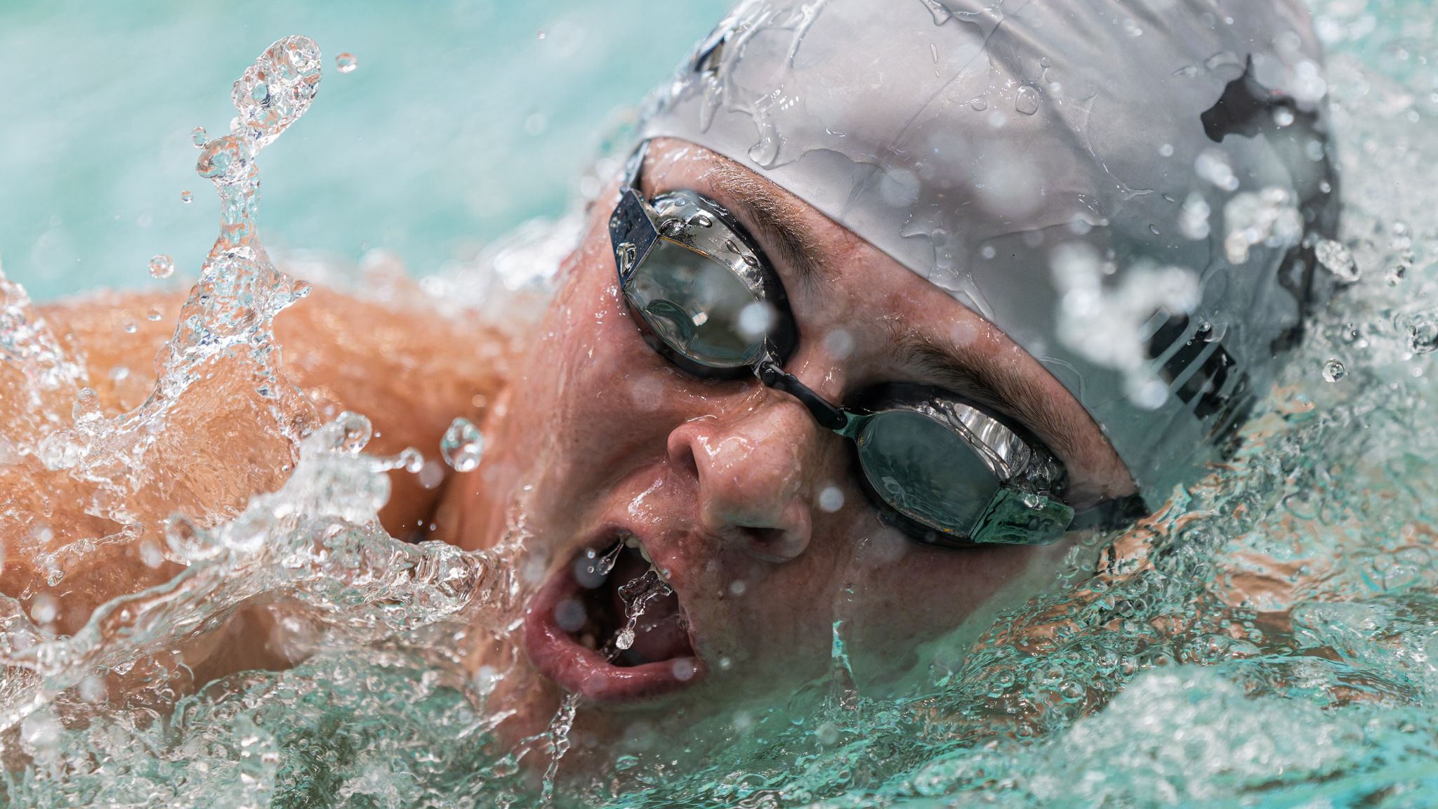 Competitive swimmer in goggles and cap powering through water during a freestyle race.