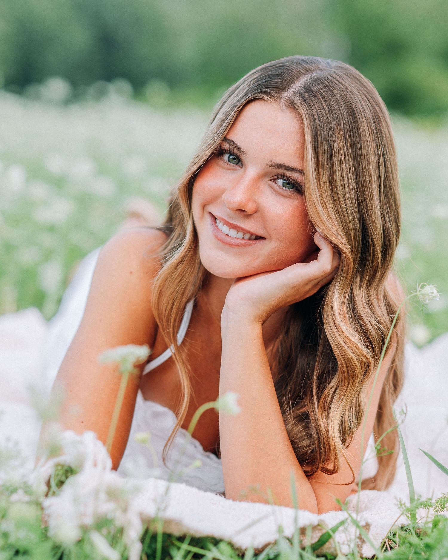 Young woman with wavy blonde hair smiling in a field of white wildflowers on a sunny day.