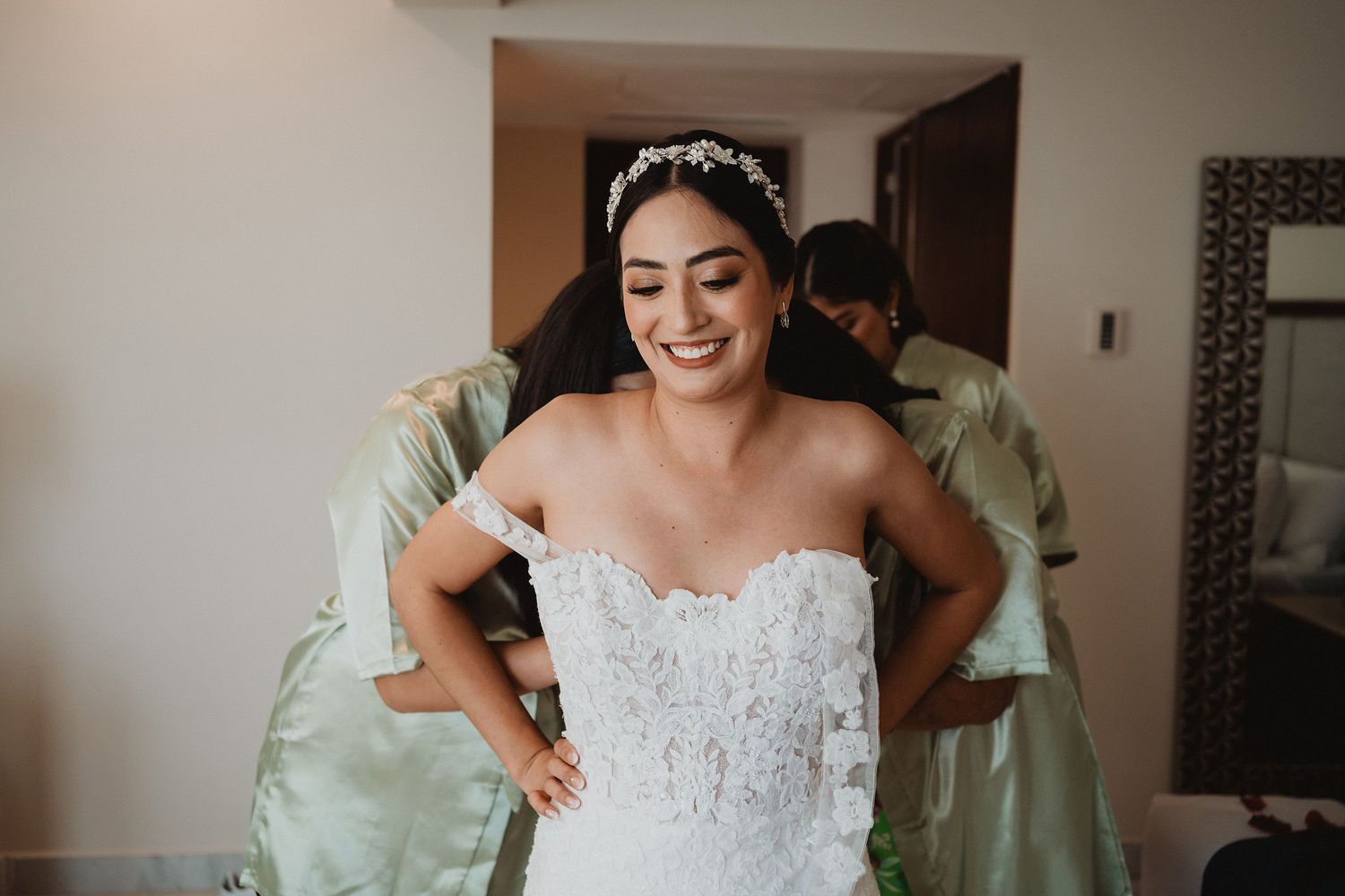 Novia sonriendo mientras le ayudan a colocar su vestido.