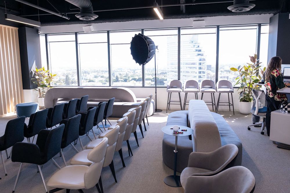 Modern conference room with rows of chairs, high bar stools, large windows, and city views in a stylish office space.