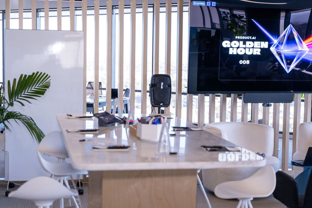 Modern conference room with white chairs, a long table, microphone, and a TV displaying Golden Hour event branding.
