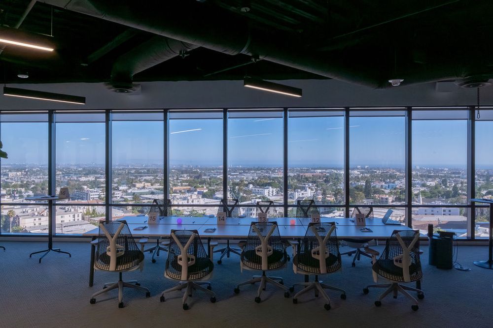 Spacious conference room with floor-to-ceiling windows offering panoramic city views, long table, and ergonomic chairs.