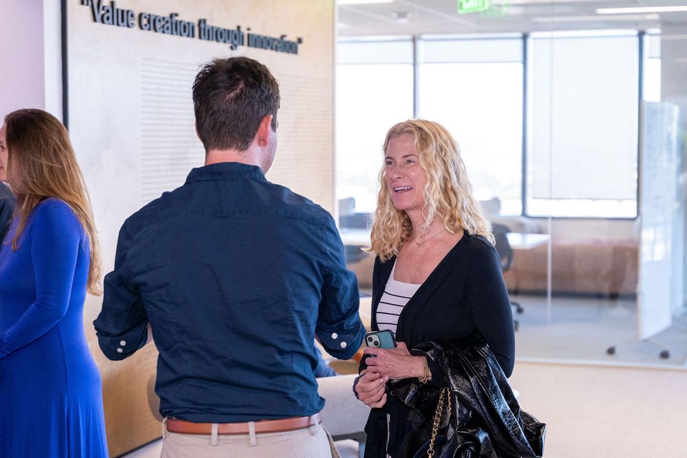 Two professionals networking in a modern office lobby beneath a Value Creation Through Innovation wall sign.